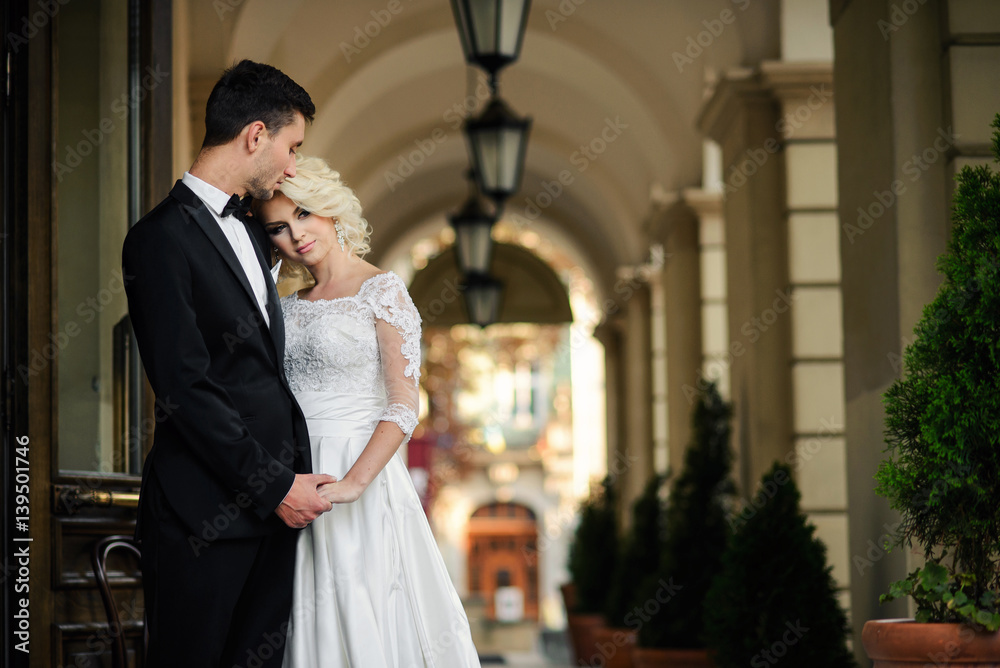 Handsome groom hugging his beautiful sensual bride against the background of the passage with arches and lanterns Handsome groom hugging his beautiful sensual bride against the background of the passage with arches and lanterns
