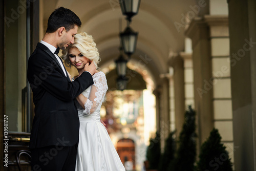 Handsome groom hugging his beautiful sensual bride against the background of the passage with arches and lanterns