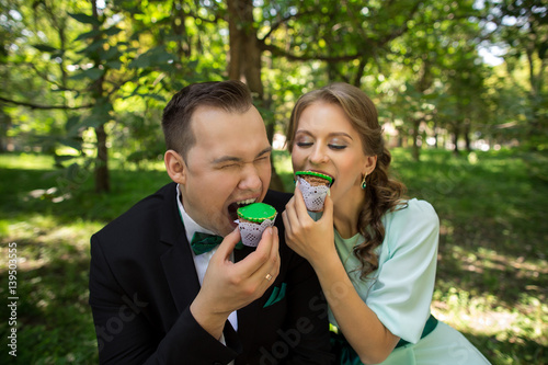 Man and woman eating green cupcakes in park. Bride and groom having fun on green wedding or saint patrick day