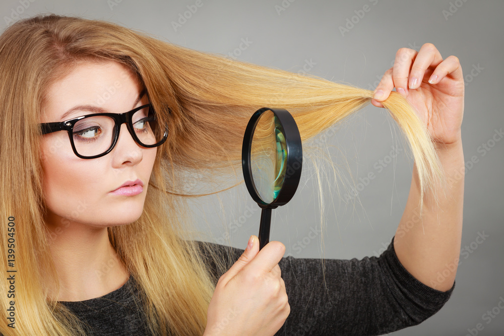 Woman holding magnifying glass looking at hair Woman holding magnifying glass looking at hair