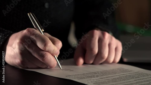 Close up shot of the hand of a grown man, who enters into a contract with a competitor company. Businessman signs pen on one of the sheets of the contract, the transfer of the company's successful.