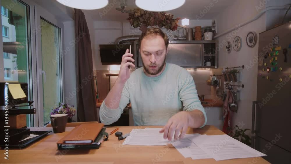 Young businessman with documents sitting at the table, working with papers and calling to someone on smartphone. Young businessman with documents sitting at the table, working with papers and calling to someone on smartphone.
