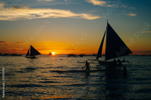 Beautiful golden sunset over fishing boats and people in water