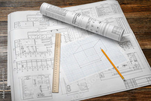 A set of open and rolled up blueprints on wooden table background with a pencil and a ruler lying beside.