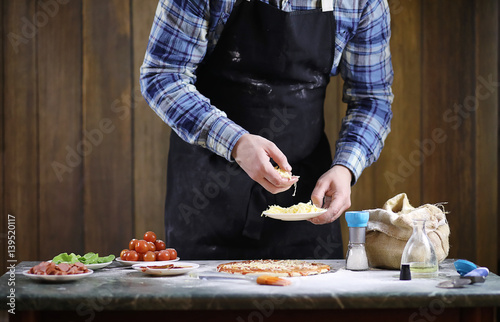 man preparing a pizza, knead the dough and puts ingredients