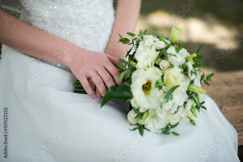 The gold ring on the bride’s finger. Wedding. Bride holds in her hands wedding bouquet with white flowers