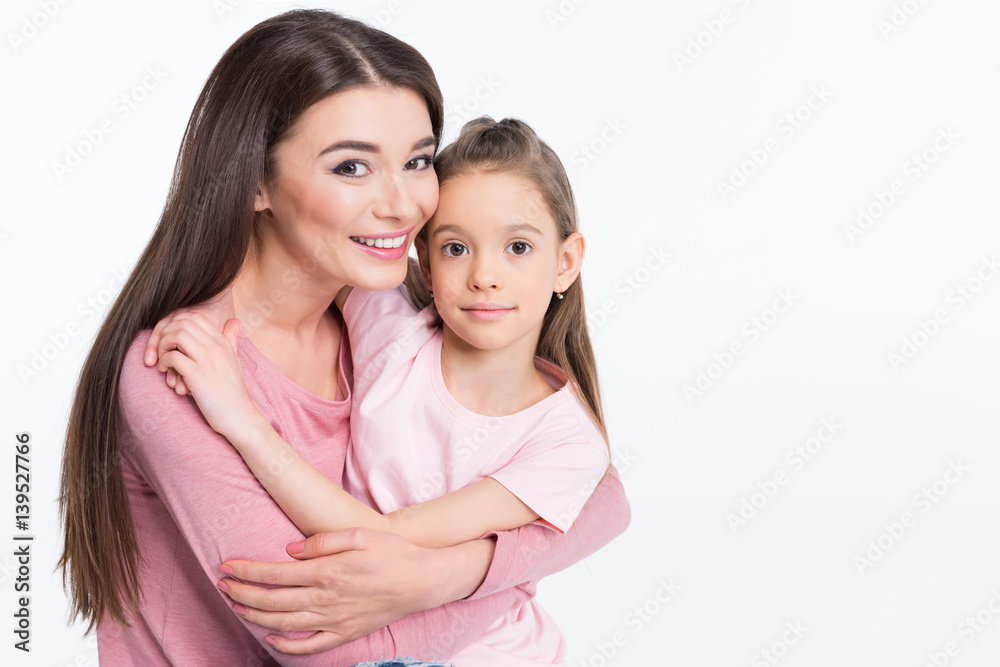 Happy mother and daughter hugging and smiling at camera on white Happy mother and daughter hugging and smiling at camera on white