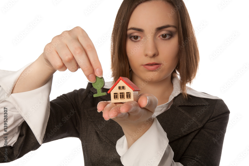 Businesswoman planting a toy tree near the toy house (focus on house) Businesswoman planting a toy tree near the toy house (focus on house)