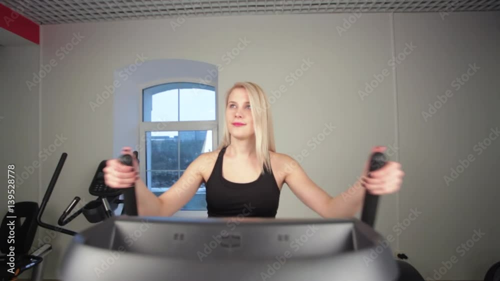 Athlete tanned blonde girl is at a gym. Exercises on the ellipsoid by working your muscles in the legs. Athlete tanned blonde girl is at a gym. Exercises on the ellipsoid by working your muscles in the legs.