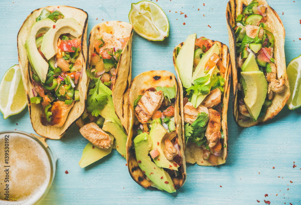 Φωτογραφία Healthy corn tortillas with grilled chicken, avocado, fresh salsa, limes and beer in glass over blue wooden background, top view