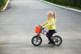 Little girl in yellow jacket on runbike. Happy child outdoors