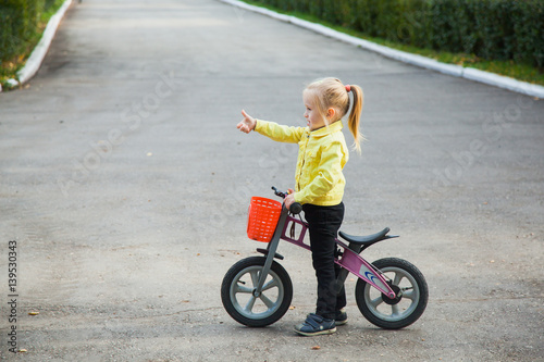 Little girl in yellow jacket on runbike with her thumb up © okfoto