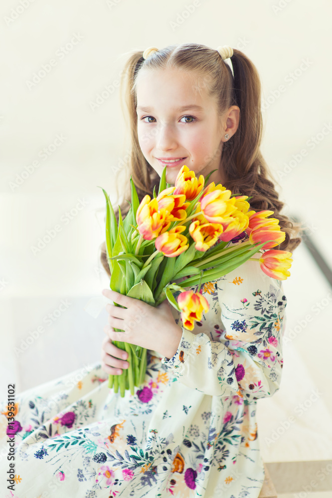 Beautiful toddler girl sitting in the room with fresh tulips, smiling with happy face, waiting for spring and Easter holidays Beautiful toddler girl sitting in the room with fresh tulips, smiling with happy face, waiting for spring and Easter holidays