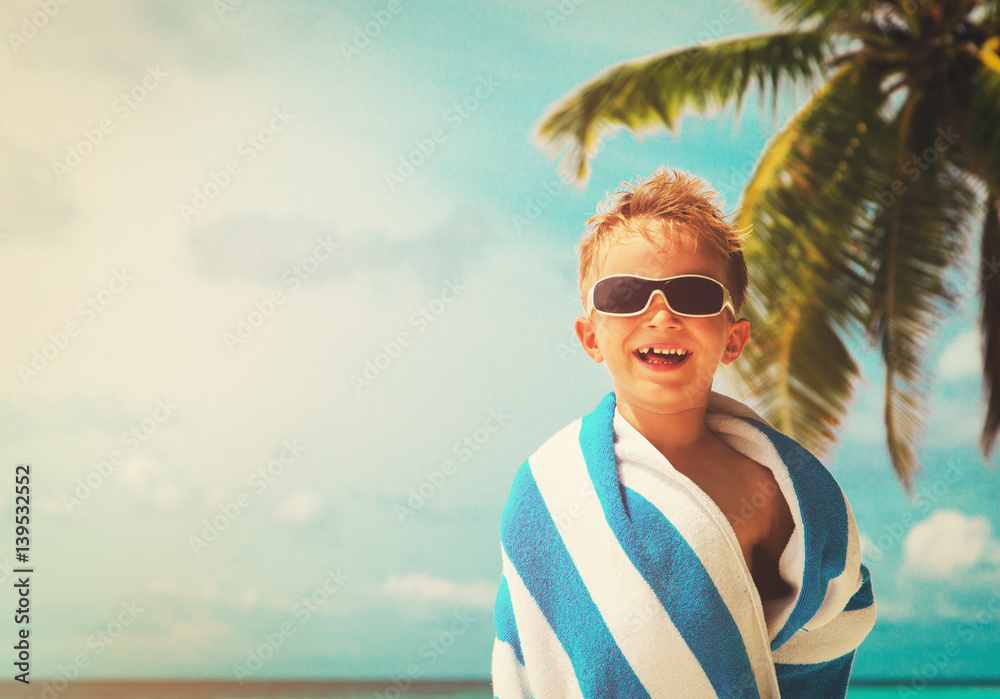 happy little boy wrapped in towel at beach