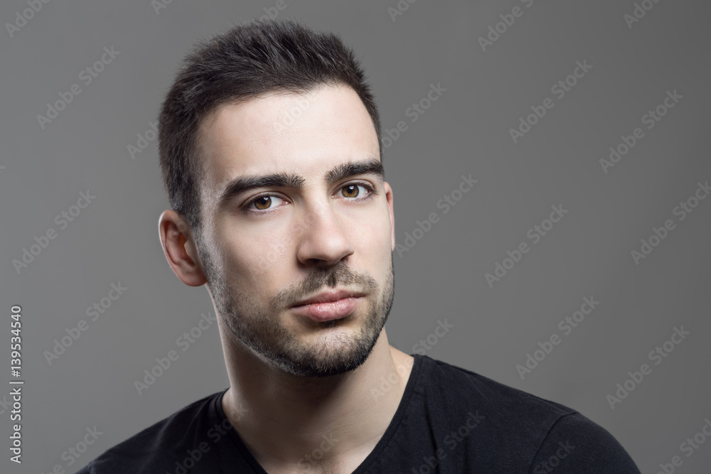 Close up moody portrait of skeptical stubble man looking at camera over dark gray studio background. Close up moody portrait of skeptical stubble man looking at camera over dark gray studio background.
