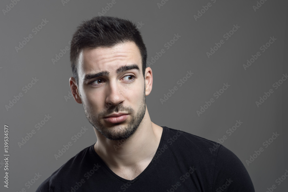 Moody portrait of confused man facial reaction looking away over dark gray studio background. Moody portrait of confused man facial reaction looking away over dark gray studio background.