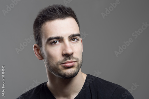 Close up moody portrait of skeptical stubble man looking at camera over dark gray studio background.