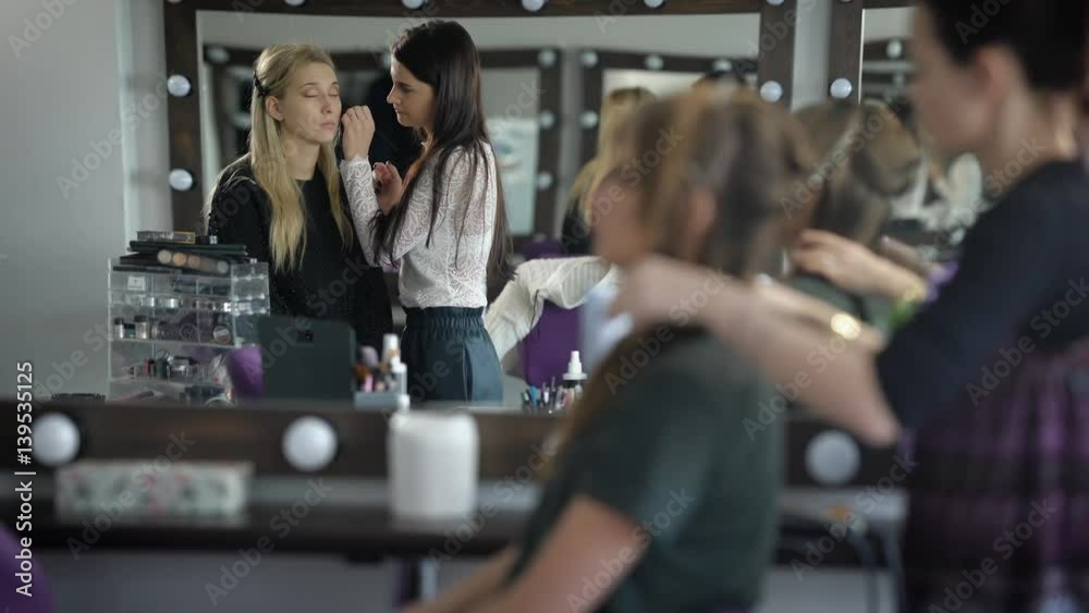 Two girlfriends in beauty shop. Girls prepare for a party. The makeup artist does a make-up to the fair-haired woman. Studio of beauty very cozy Two girlfriends in beauty shop. Girls prepare for a party. The makeup artist does a make-up to the fair-haired woman. Studio of beauty very cozy