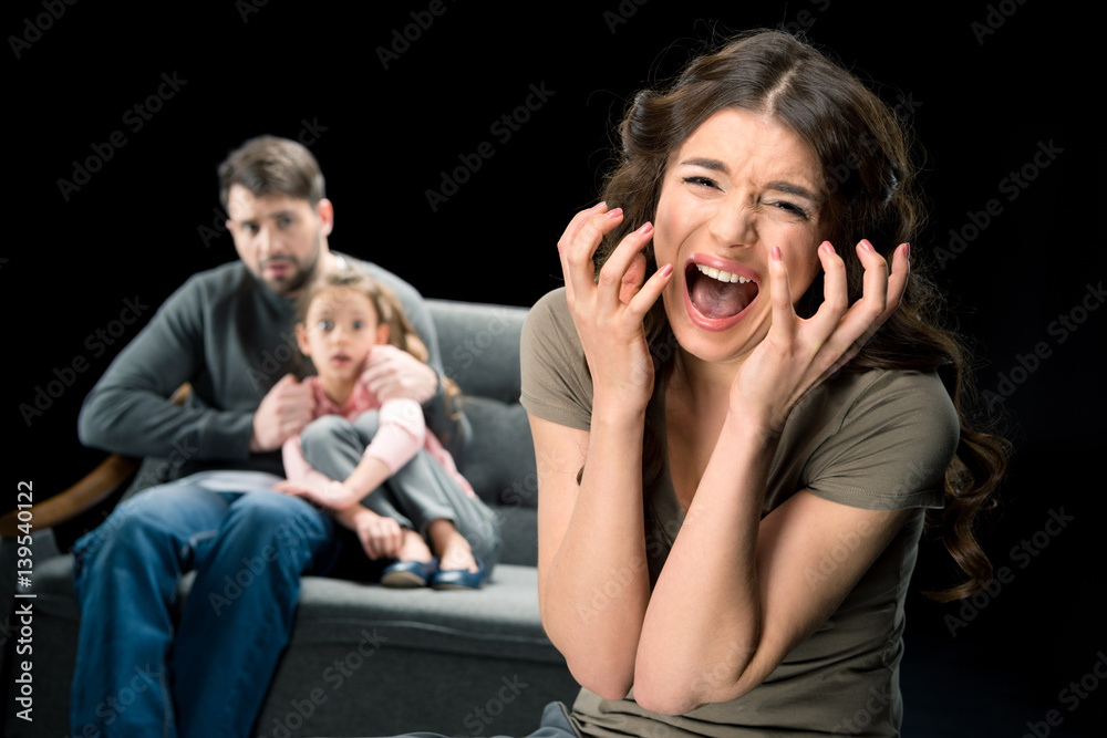 Scared girl sitting with father on couch while mother screaming at camera, family problems concept