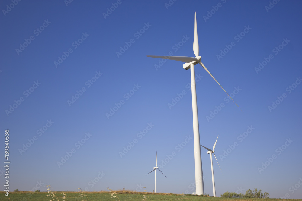 View of windmills towers from the ground with a cloudless blue sky.