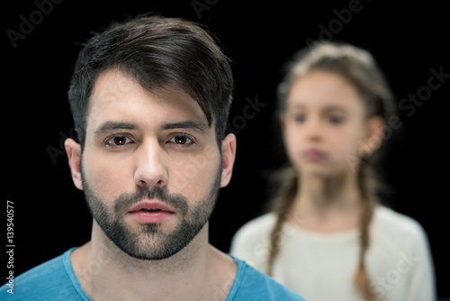 portrait of bearded man with little girl behind on black