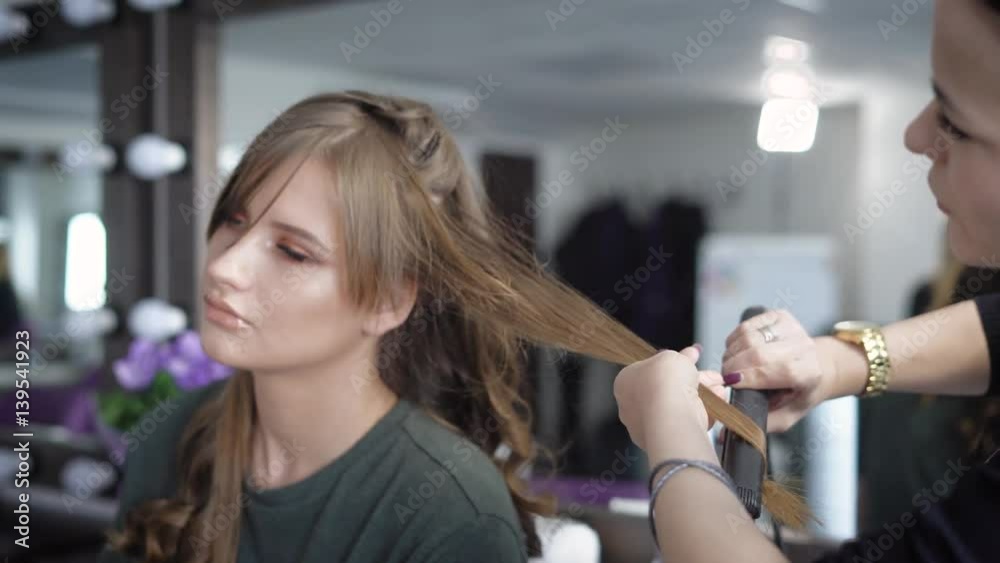 Hairdressing salon. The specialist in hair stacks the girl on a party. The hairdresser does ringlets by means of the special curling iron. Hairdressing salon. The specialist in hair stacks the girl on a party. The hairdresser does ringlets by means of the special curling iron.