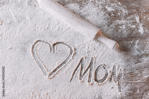 'Top view of heart symbol and word mom in flour on wooden table, Mothers day concept