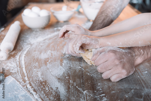 'Close-up partial view of father and daughter kneading dough together