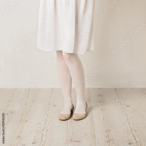 Female legs in white tights, skirt and ballet flats on a white background.