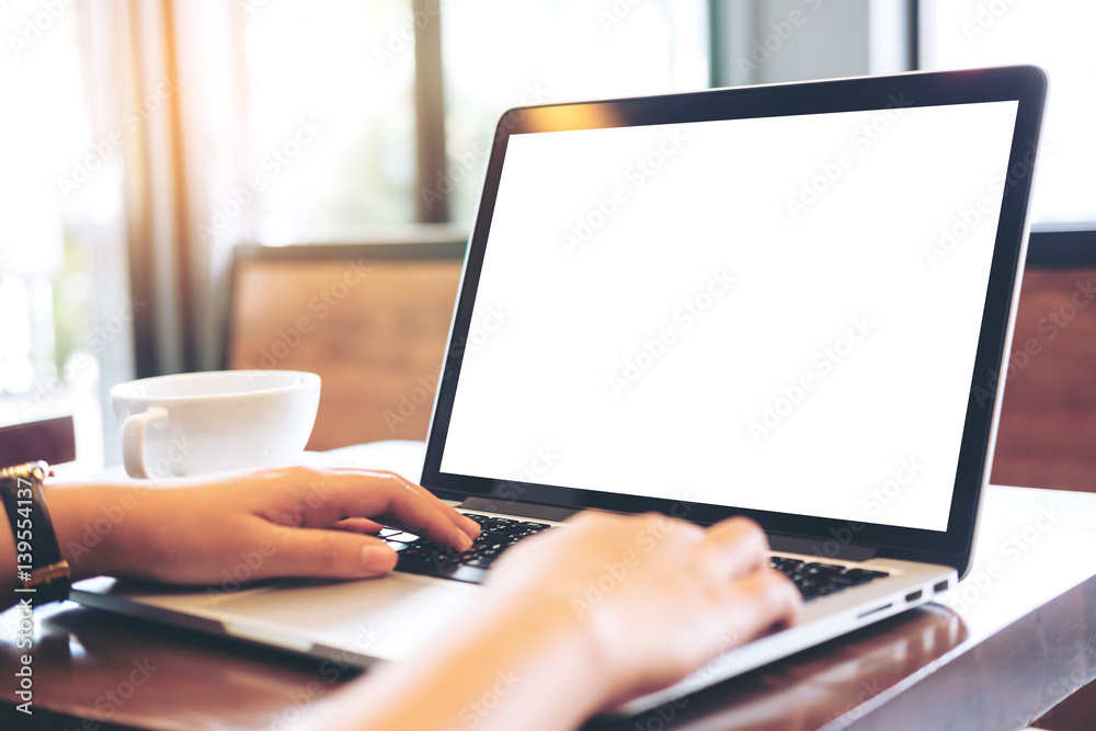 Mockup image of hands using laptop with blank white screen on vintage wooden table in cafe Mockup image of hands using laptop with blank white screen on vintage wooden table in cafe
