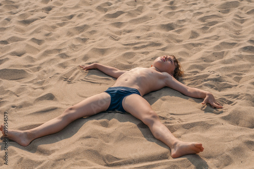 Boy lying on the beach apart arms and legs