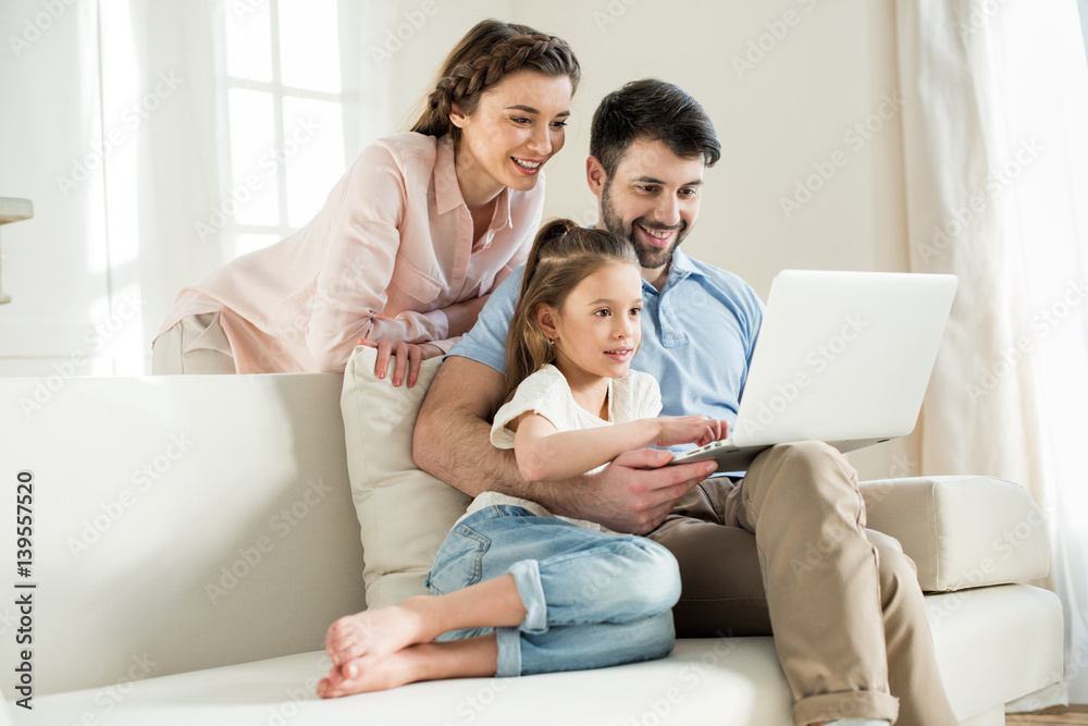 smiing parents and focused daughter using laptop at home smiing parents and focused daughter using laptop at home