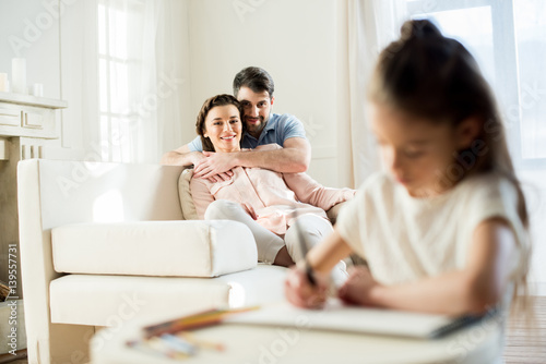 smiling parents watching daughter drawing picture at home