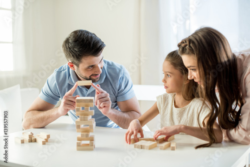 portrait of concentrated parents playing jenga game with daughter