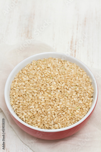 raw rice in red bowl on wooden background