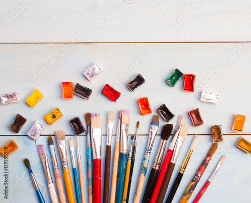 Paints, brushes on the white wood background. The workplace of the artist. Banner for school