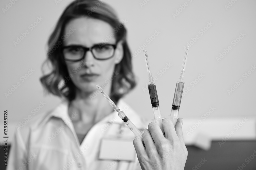 Serious woman doctor holding syringes and looking at camera, black and white photo Serious woman doctor holding syringes and looking at camera, black and white photo