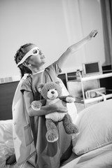 Black and white photo of little girl superhero playing with teddy bear i hospital