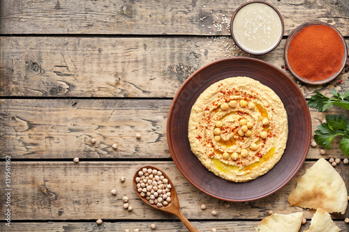 Hummus traditional homemade eastern snack chickpea vegan natural nutrition dip paste with paprika tahini parsley and olive oil in clay plate on rustic flat lay. Healthy dietary fiber protein food