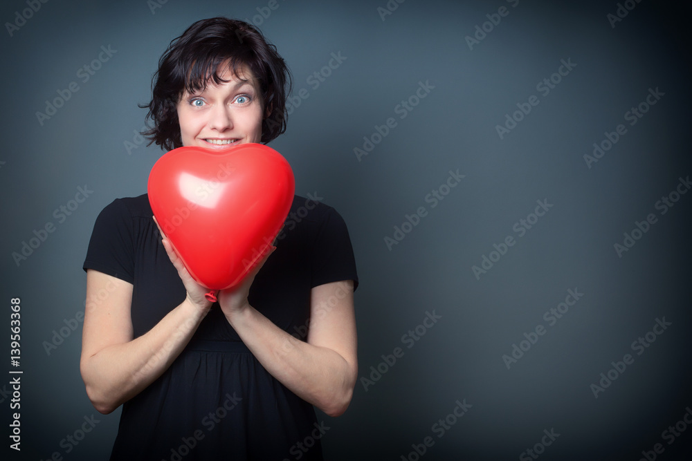 Beautiful Surprised Woman, holding a Red Heart Balloon, on Grey Background with Copy Space Beautiful Surprised Woman, holding a Red Heart Balloon, on Grey Background with Copy Space