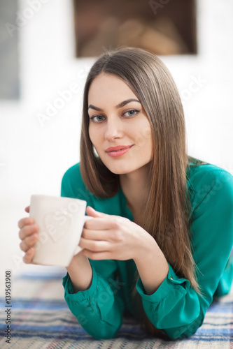 Young beautiful woman lying on plaid with cup of hot coffee in home
