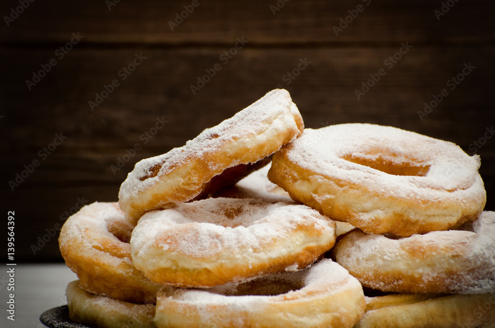 Donuts sprinkled with powdered sugar, dark wood background. Close-up, side view