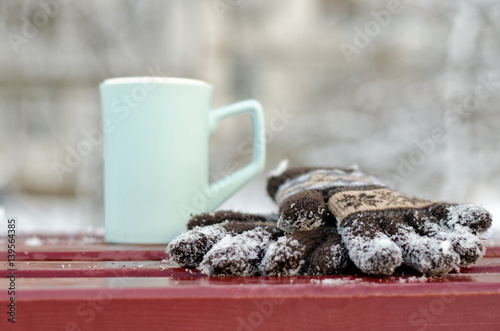 Blue a mug and women's knitted gloves on a bench in the winterd. Close-up photo