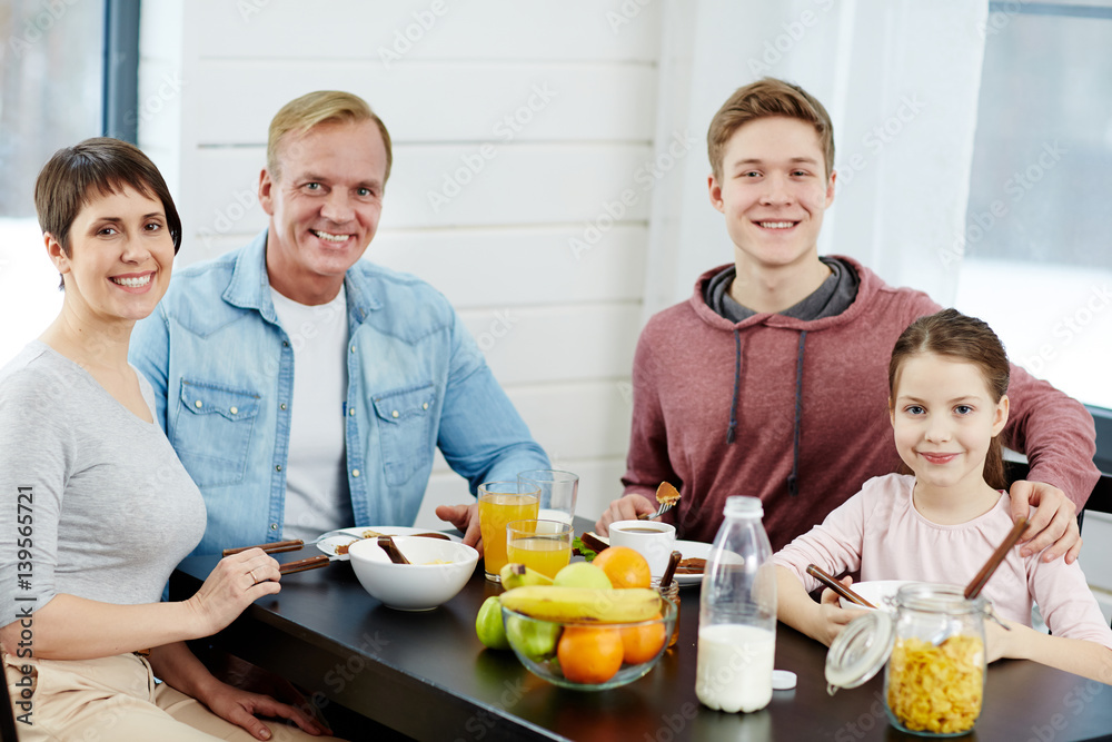 Cheerful family sitting by table with healthy organic food