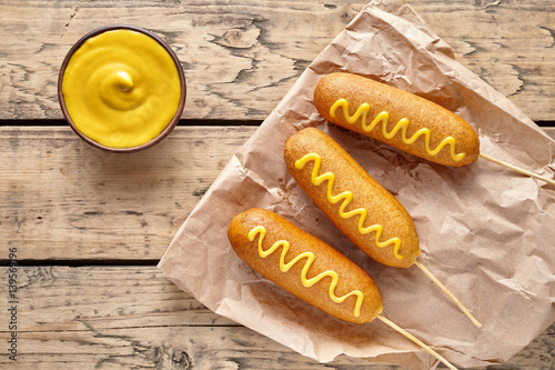 Sticker Corn dog traditional American street junk food deep fried hot dog meat sausage with mustard snack treat coated in a thick layer of cornmeal batter on stick unhealthy eating on rustic wooden desk