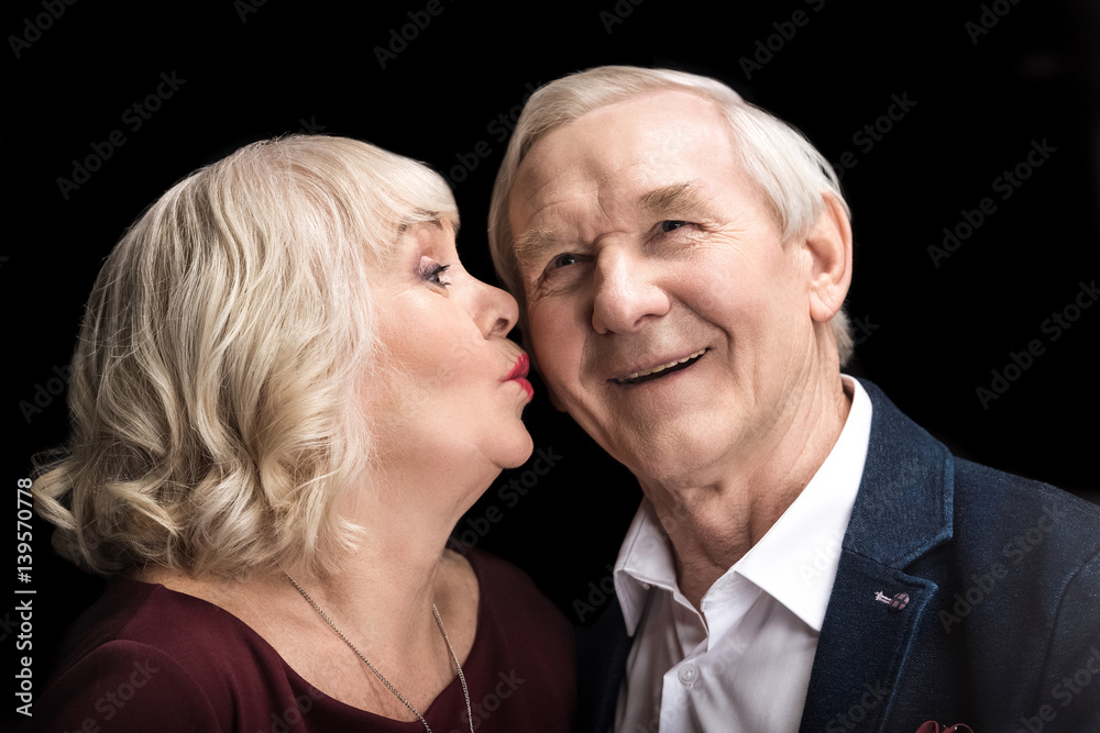Beautiful senior woman kissing happy man on black Beautiful senior woman kissing happy man on black