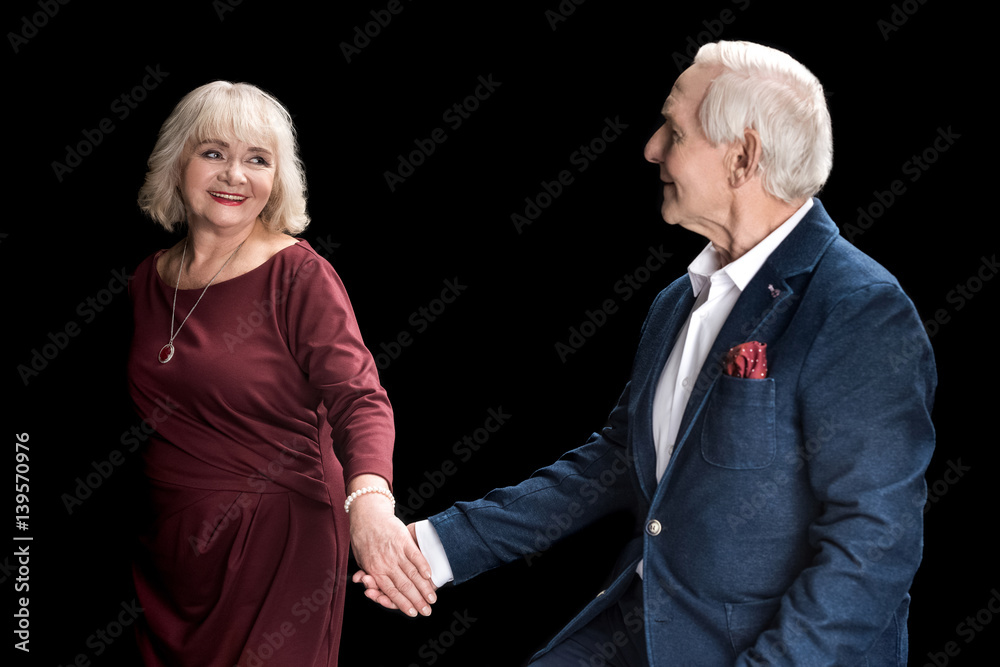 Happy senior couple holding hands and looking at each other on black