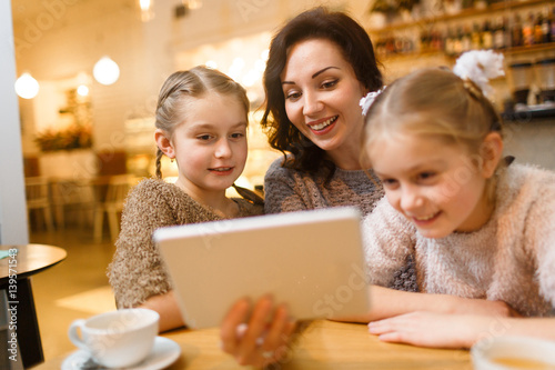 Happy young woman with touchpad showing her twin daughters movie for children