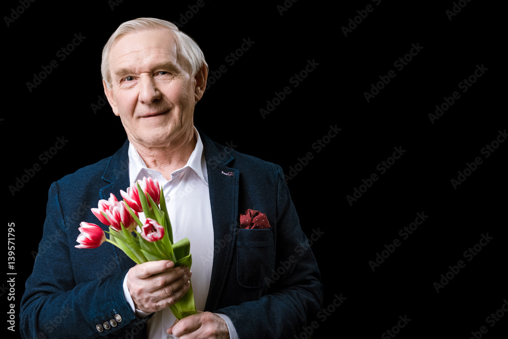 Senior man in suit holding tulips bouquet and smiling at camera, spring holiday concept Senior man in suit holding tulips bouquet and smiling at camera, spring holiday concept