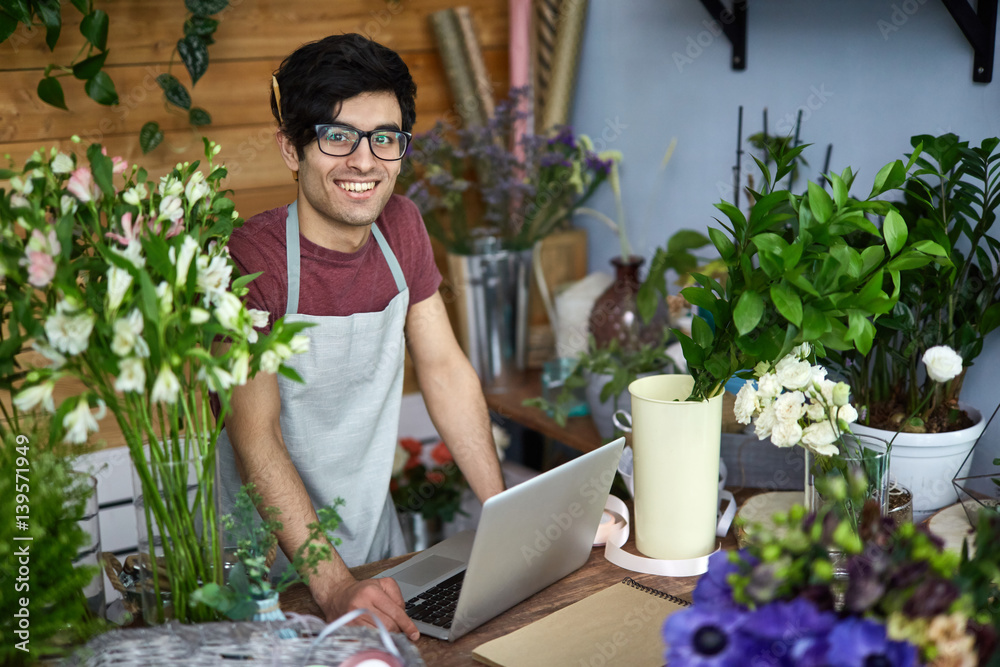 Happy young florist by counter looking at camera Happy young florist by counter looking at camera